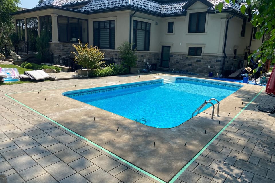 Large pool deck before resurfacing: faded, weathered tan concrete around a stone house