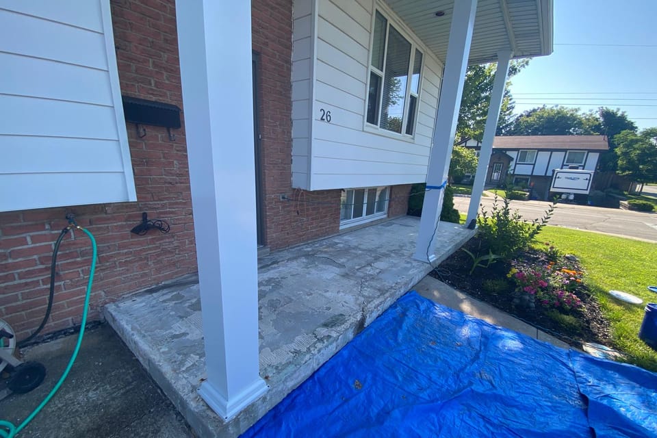 Front porch before resurfacing: spalled, patched and discoloured concrete between white columns