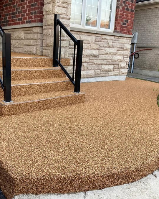 A curved honey-gold Gator Grip front patio and steps beside a stone-clad house